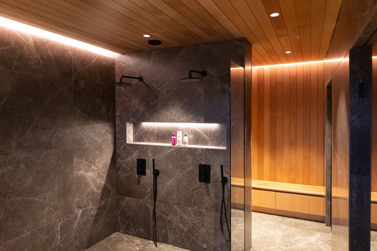 Illuminazione del bagno e dello spogliatoio con faretti a incasso e strisce LED indirette lungo il soffitto. Inoltre, il ripiano dello shampoo è illuminato da una striscia LED in un profilo compatto di alluminio.